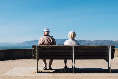 An elderly couple sits on a bench overlooking rolling hills