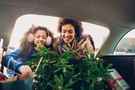 Mother and daughter putting a fresh Christmas tree in the car.