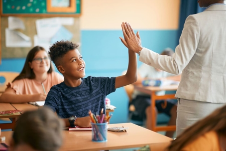 Boy smiling in school room giving teacher a high five.