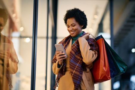 Happy woman checking her phone while holiday shopping.
