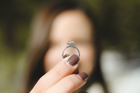 A woman with manicured fingernails holds up an engagement ring
